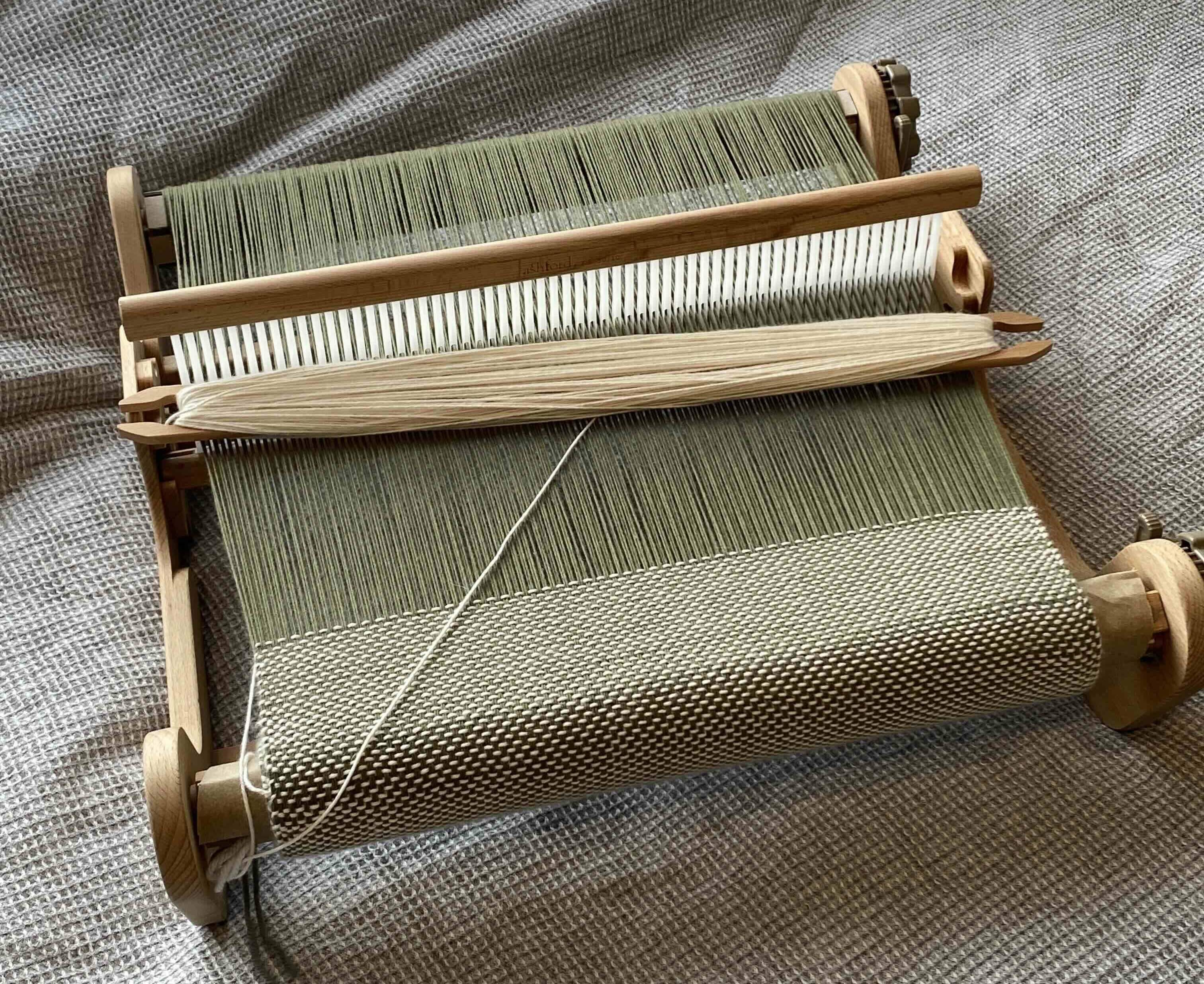 A rigid heddle loom with green warp thread and white weft thread